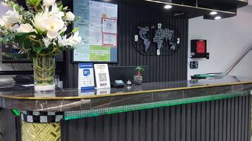 A reception desk with a black and gold design, a vase of white flowers, a digital screen, and a wall with country names.