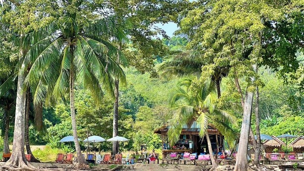 A beach with palm trees, a thatched-roof hut, and beach chairs. - Three ladies (Ko Yao)