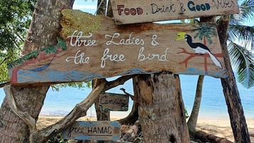 Uma placa de madeira com várias mensagens, incluindo 'Comida, Bebida e Boas Vibrações', 'Three Ladies & The Free Bird' e 'Rede Livre'.
