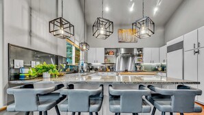 Une cuisine moderne dotée d’un îlot central, de tabourets de bar, de luminaires suspendus et d’appareils électroménagers en acier inoxydable.