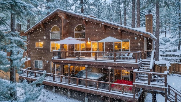 Une cabane en rondins dotée d’un balcon et de nombreuses fenêtres, entourée d’arbres couverts de neige.