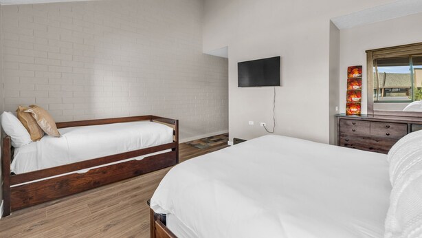 Un dormitorio con dos camas de madera, un televisor de pantalla plana montado en la pared y un aparador con espejo.