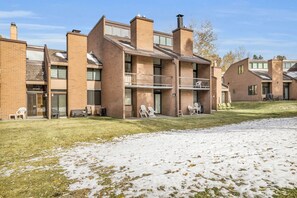 A multi-story brick building with balconies, outdoor seating, and a grassy area with some snow. - Park City Golf Course Condo: Pool & Hot Tub Access (Park City)