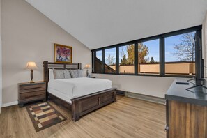A bedroom with a large bed, wooden headboard, two bedside tables with lamps, a rug, and a view of the outside through a large window. - Park City Golf Course Condo: Pool & Hot Tub Access (Park City)