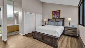 Un dormitorio con cama de madera, dos mesitas de noche con lámparas, un cuadro en la pared y vistas al exterior.