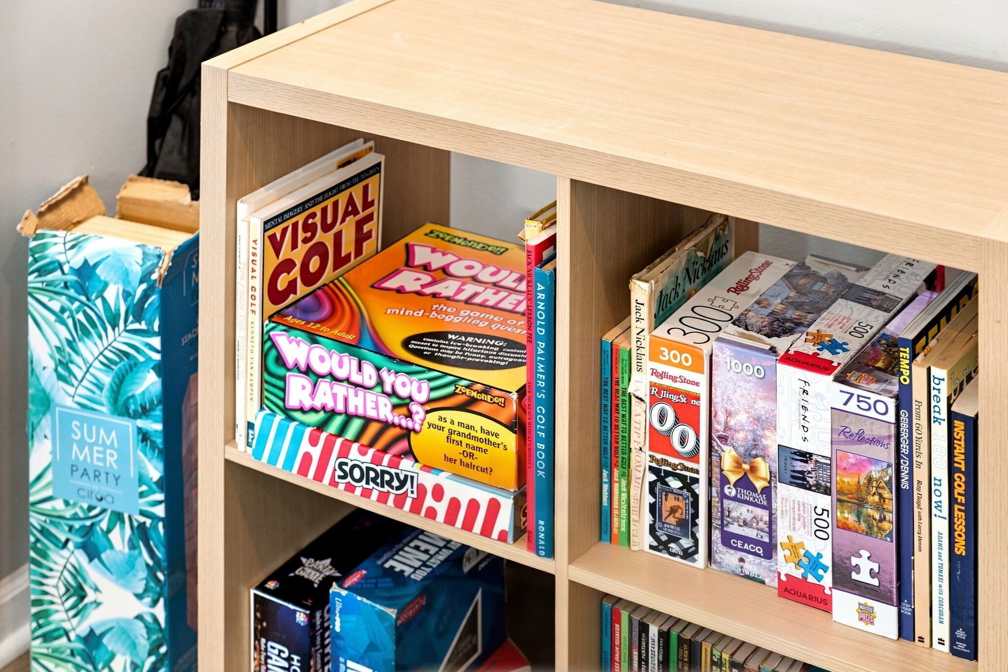 Een boekenkast met verschillende boeken en spelletjes, waaronder een 'Visual Golf' spel en een 'Would You Rather?' spel.