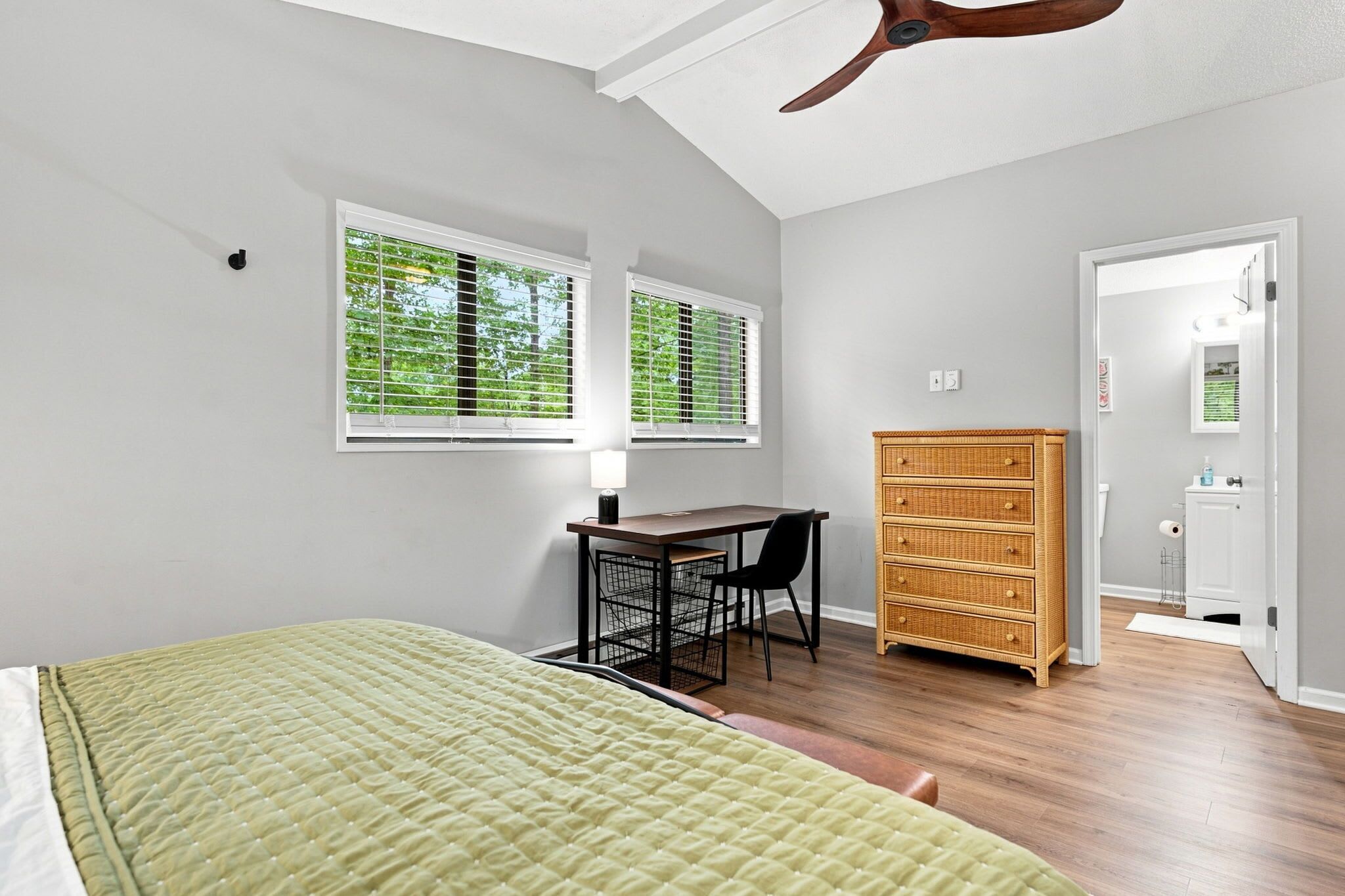 A bedroom with a bed, a desk, a chair, a dresser, and a window with blinds.