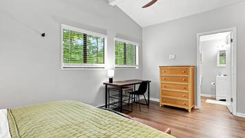 A bedroom with a bed, a desk, a chair, a dresser, and a window with blinds.