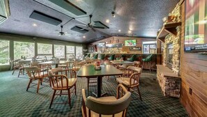 Un restaurante con varias mesas y sillas, una zona de bar y una pantalla de televisión.