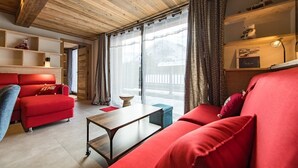 A cozy living room with red sofas, a wooden ceiling, and a view of the outdoors. - New apartment in resort center - sleeps 8/9 (ST SORLIN D ARVES)