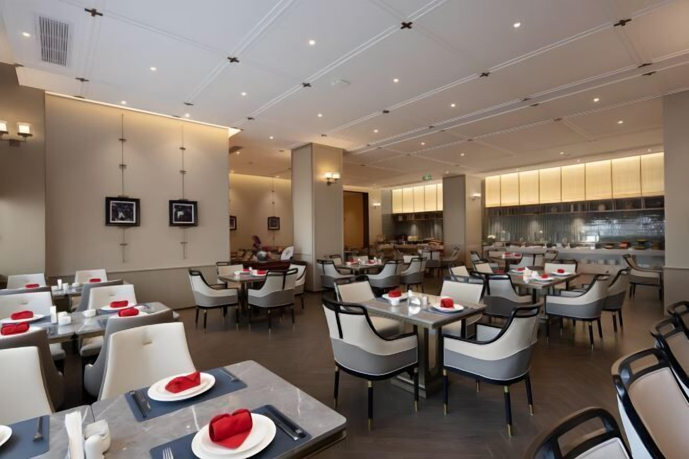 A modern dining area with tables and chairs, a kitchen in the background, and a clean, contemporary design.