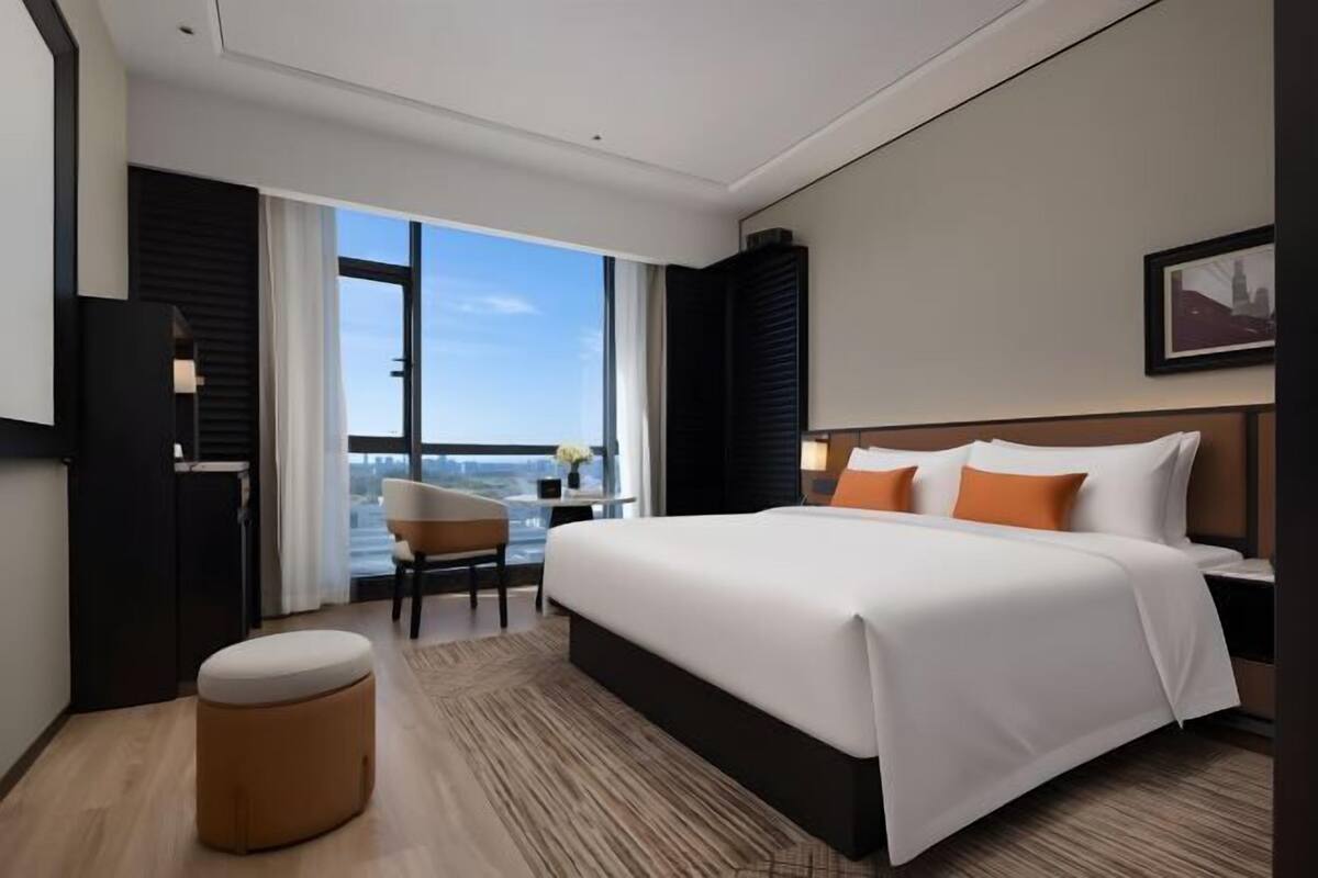 A modern hotel room with a large bed, a seating area, and a view of the city.