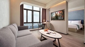 Une chambre d’hôtel moderne, dotée d’un canapé, d’une petite table avec un livre, d’un lit et d’une grande fenêtre donnant sur la ville.