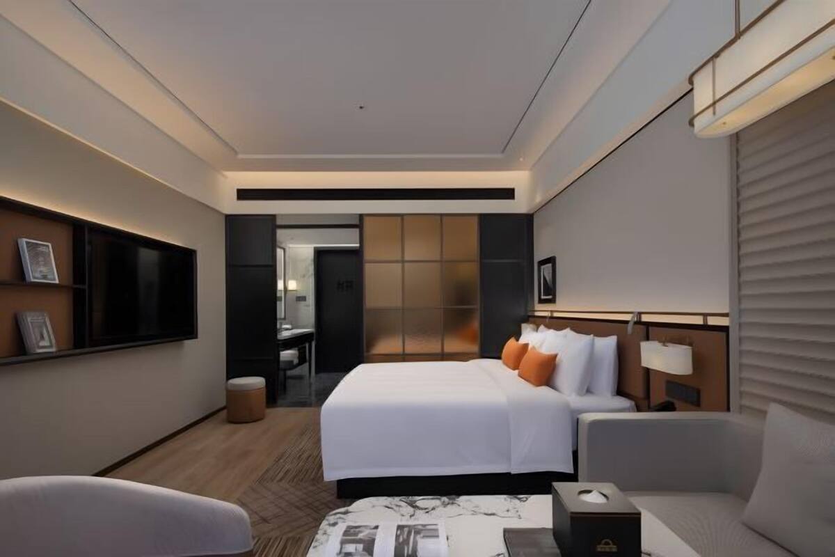 A modern hotel room with a large bed, bedside tables, a flat-screen TV, and a seating area.
