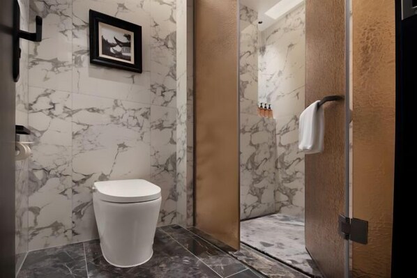 Un baño con inodoro, paredes de mármol y zona de ducha.