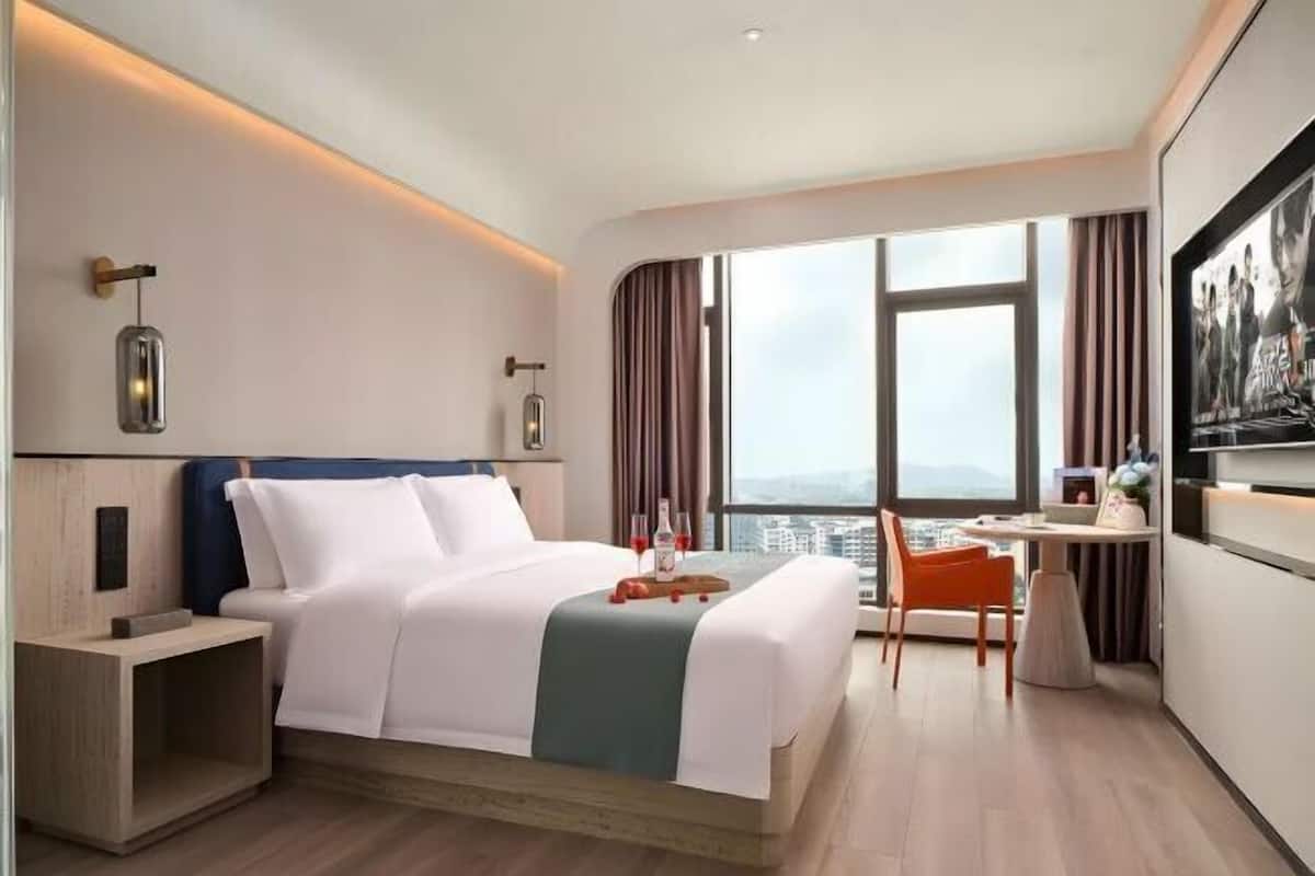 A modern hotel room with a large bed, a desk, and a view of the city.