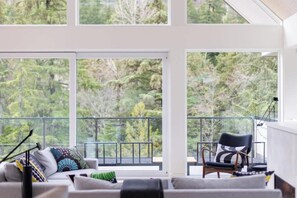 A modern living room with large windows, a sofa, a chair, and a balcony with a railing. - Private Scandinavian Chalet, Mountain views (Whistler)