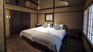 A hotel room with a large bed, a small bedside table, a window with a view, and a wooden ceiling. - Onju Kamikyo (Kyoto)