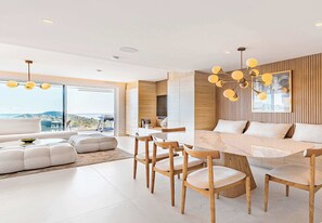 A modern living room with a large sofa, dining table, and chairs, a kitchen area, and large windows with a view. - Palo Alto 3 | Marbella Luxury Modern Views (Málaga)