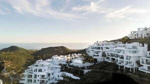 Ein Küstenwohngebiet mit modernen weißen Gebäuden, freiem Blick auf das Meer und einer hügeligen Landschaft.