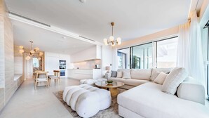 Ein modernes Wohnzimmer mit einer großen Couch, Hockern, einem Couchtisch und einem Essbereich mit Stühlen.