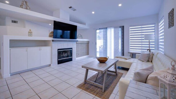 Una sala moderna con sofá, una mesa de centro, chimenea y una zona de cocina con armarios y televisor.