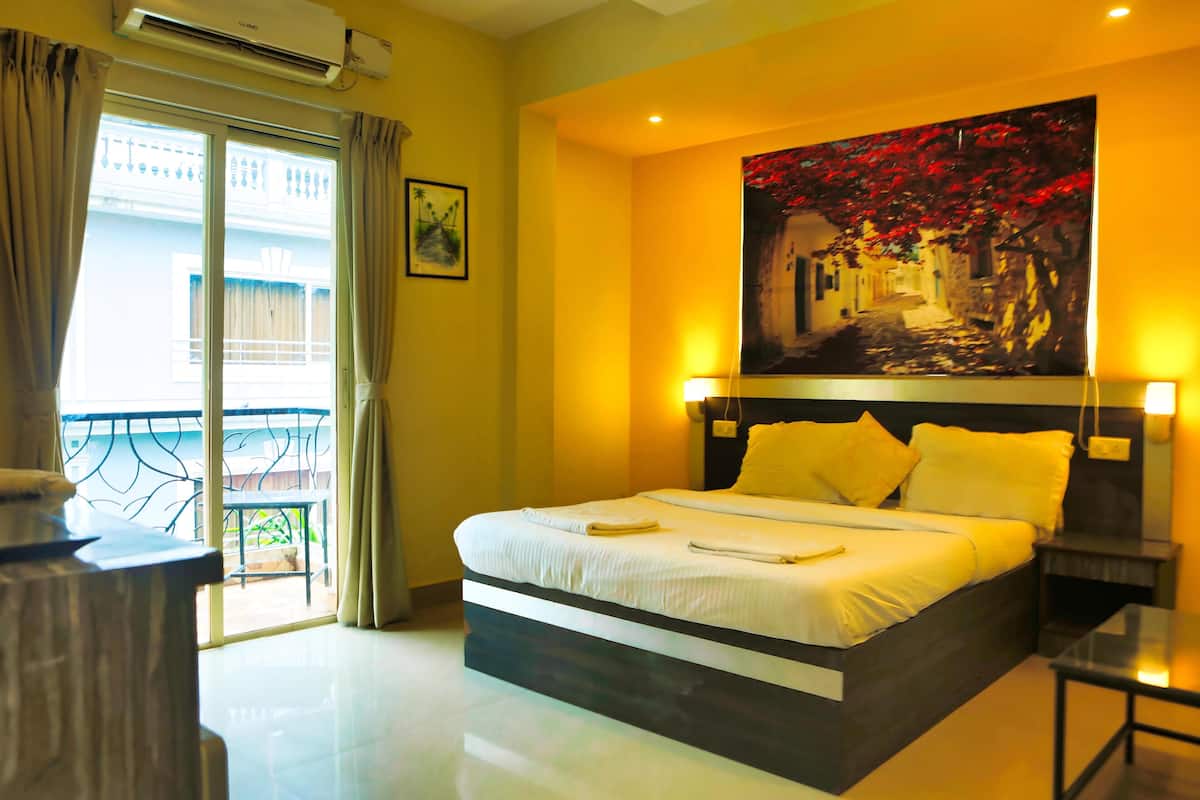 A hotel room with a large bed, a balcony with a view, and a painting on the wall.
