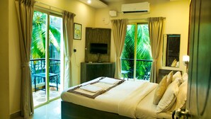 A bedroom with a bed, a TV, a balcony with chairs, and a view of palm trees. - Daksh Elite Candolim Goa (Candolim)