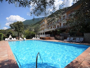 Une piscine à l’eau d’un bleu cristallin, entourée de chaises longues blanches et bordée d’un bâtiment doté de balcons.