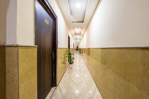 A hallway with a marble floor, a wooden door with a number sign, and potted plants. - Hotel Kiara Delhi Airport (New Delhi)