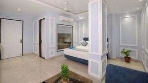 A hotel room with a large bed, a bathroom with a glass shower enclosure, a ceiling fan, and a potted plant. - Hotel Anchorage Delhi IGI Airport (New Delhi)