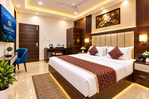 A hotel room with a bed, bedside table, lamp, desk, chair, and a TV. - Hotel Kiara Delhi Airport (New Delhi)