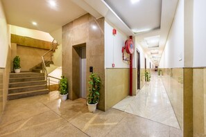 A hotel corridor with a marble floor, a staircase, and potted plants. - Hotel Kiara Delhi Airport (New Delhi)