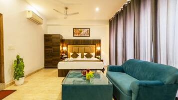 A hotel room with a bed, a sofa, a glass coffee table, a potted plant, and a ceiling fan.