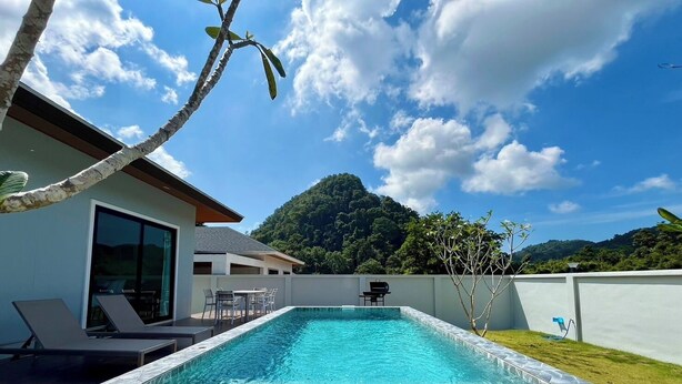 A rectangular swimming pool with a tiled edge, surrounded by a white wall and a grassy area. - Unchan Livliness Pool Villa  (Tambon Ao Nang)