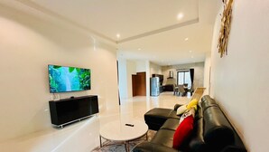 A modern living room with a flat-screen TV, black leather sofa, and a small round coffee table. - Unchan Livliness Pool Villa  (Tambon Ao Nang)