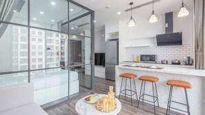 A modern kitchen with a large island, bar stools, and a dining area with a glass partition. - Coco Apartment Dcapital Luxury (Hanoi)