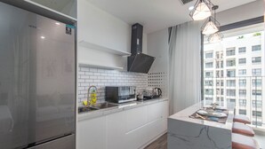 A modern kitchen with a stainless steel refrigerator, white cabinets, a black range hood, and a window with a view of buildings. - Coco Apartment Dcapital Luxury (Hanoi)