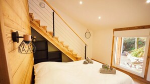 Un dormitorio con escaleras de madera, un ventanal grande y una cama con ropa blanca.