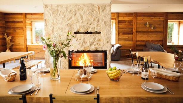 Comedor con chimenea de piedra, paredes de madera y una mesa lista para comer.