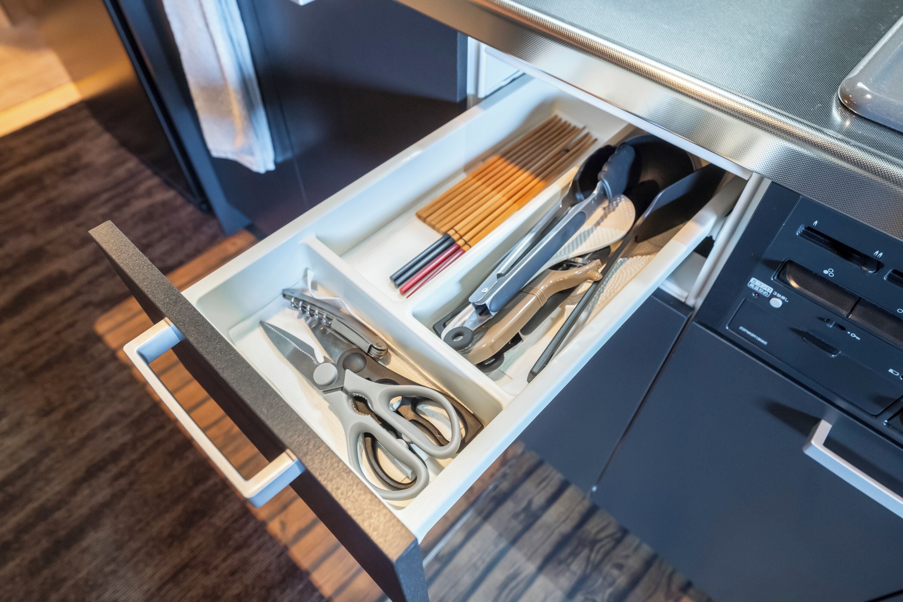 A drawer with various kitchen utensils including scissors, chopsticks, and a spatula.