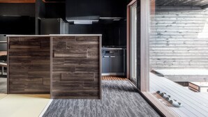 A modern kitchen with dark cabinetry, a built-in oven, and a large window overlooking a wooden deck. - THE VILLA SEIFUMEIGETSU (Shiraoi)
