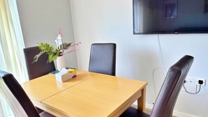 Een vergaderruimte met een houten tafel, zwarte stoelen, een vaas met bloemen en een televisie aan de muur.