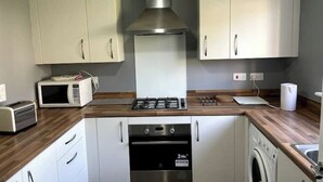Een kleine keuken met witte kastjes, een magnetron, een gasfornuis, een oven en een wasmachine.