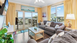 A spacious living room with a balcony, a ceiling fan, and a large window with curtains. - Crystal Tower 409 (Gulf Shores)