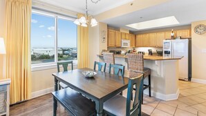A modern kitchen with wooden cabinets, a central island, and a dining area with a table and chairs. - Crystal Tower 409 (Gulf Shores)