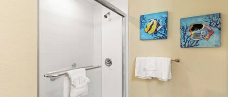 A bathroom with a glass shower door, white tiled walls, and two wall-mounted paintings of fish.