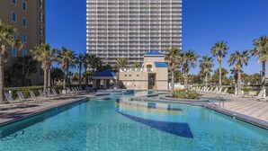 A hotel pool area with lounge chairs, palm trees, and a large building in the background. - Crystal Tower 409 (Gulf Shores)