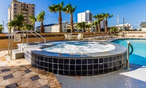 A hot tub surrounded by a pool, palm trees, and a building with a sign indicating spa rules. - Crystal Tower 409 (Gulf Shores)