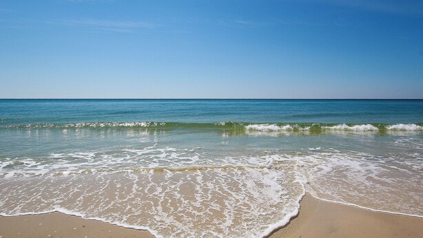 A beach with clear blue water and waves gently lapping at the shore. - Crystal Tower 409 (Gulf Shores)